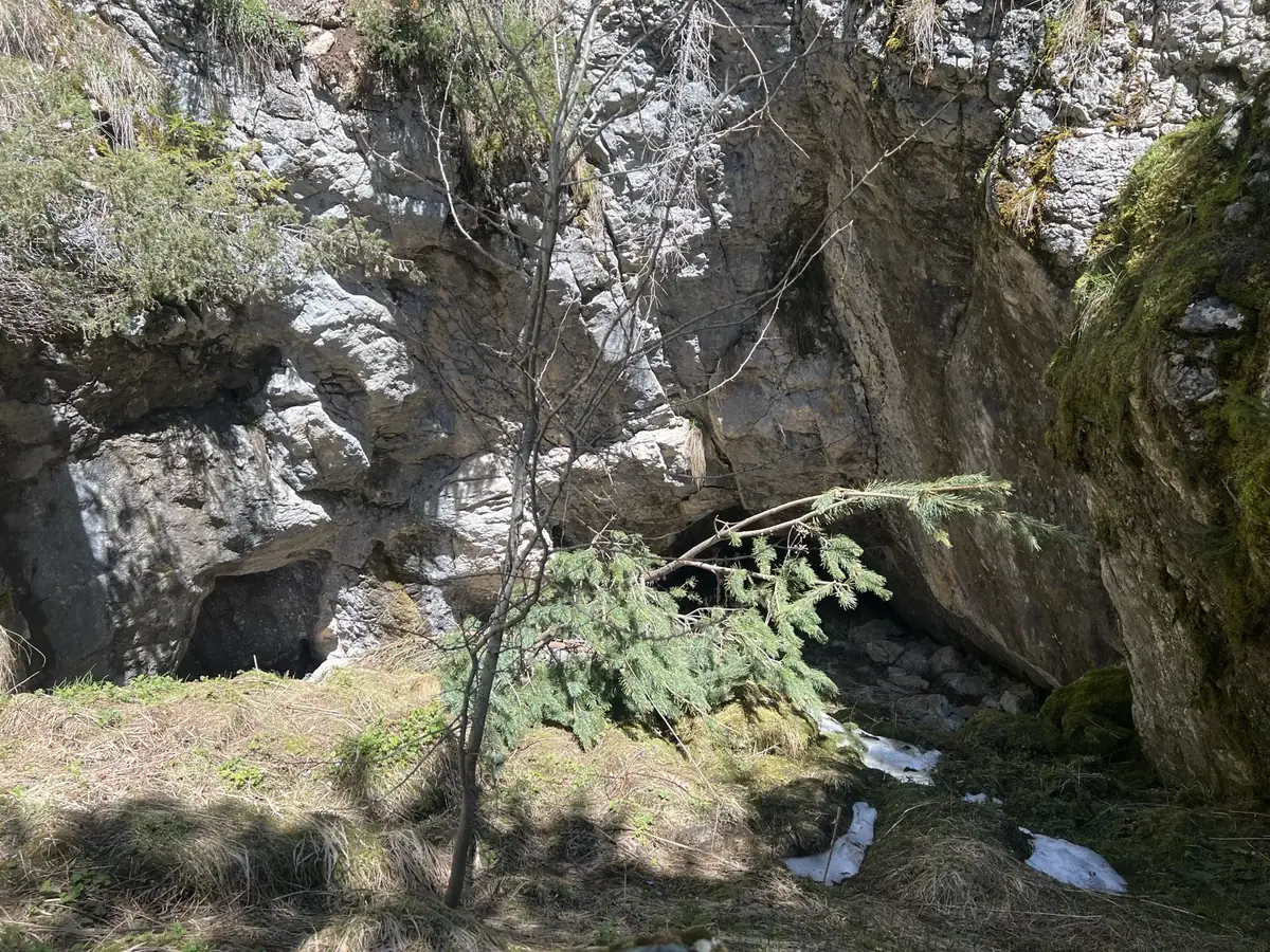 Rocky cave entrance in the hillside with patches of snow